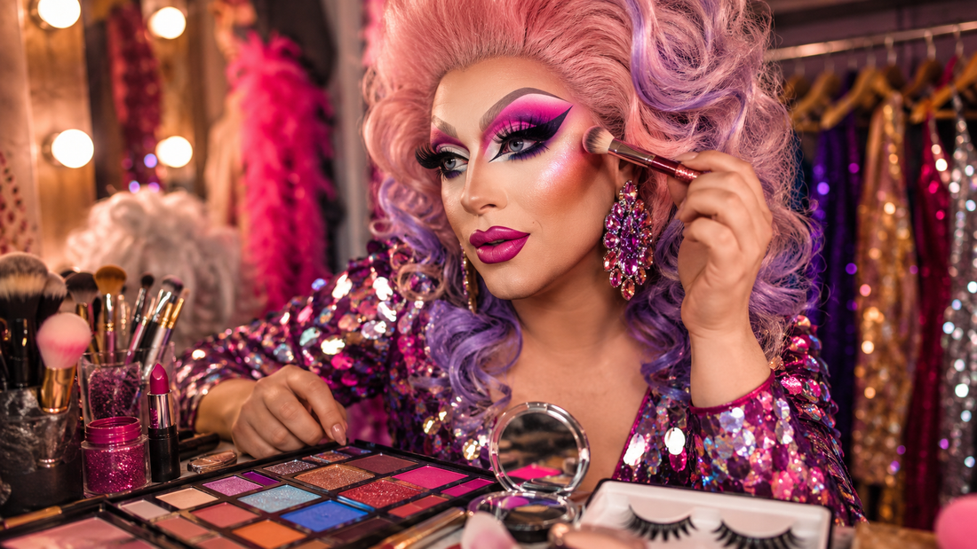 Drag queen makeup beginner setup with colorful eyeshadow palettes, brushes, lashes, lipsticks and a glamorous performer preparing a bold look.
