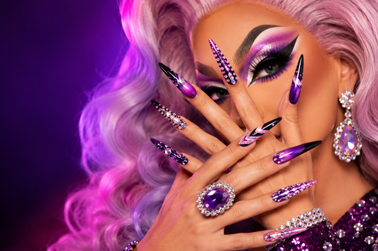 Drag queen with glamorous makeup and long false nails posing in a vanity dressing room with stage lights.